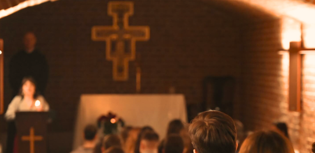 Kaplica z ceglaną ścianą, drewnianym krzyżem i ciepłym oświetleniem